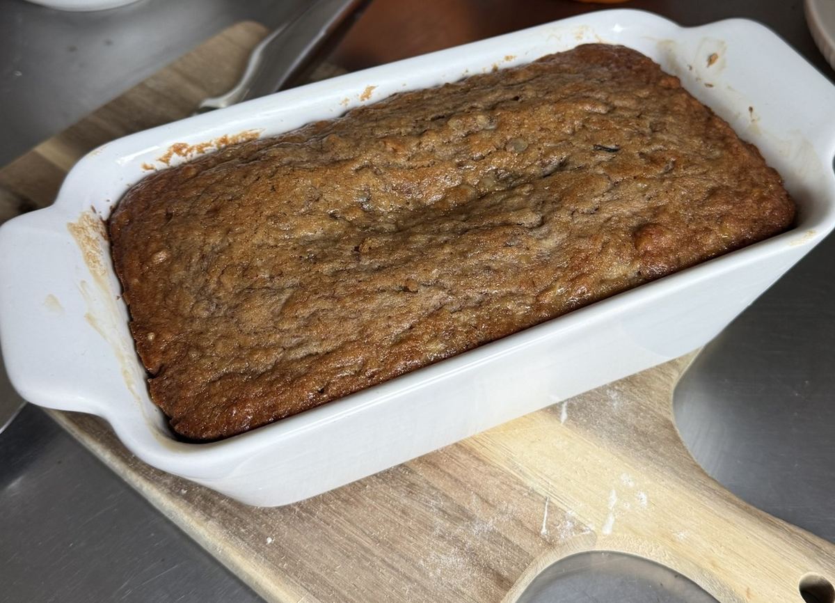 Walnut banana bread baked in a white ceramic loaf dish, with small pie pumpkins beside it