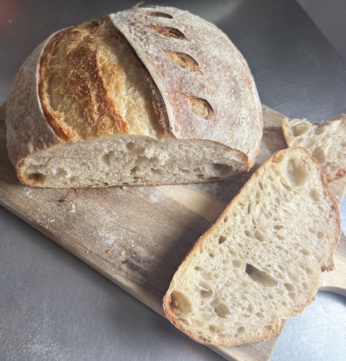 Country loaf cut in half showing an open, airy crumb, with a thick slice laid on the wooden board beside it