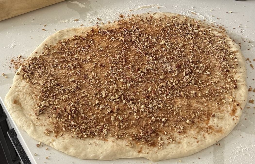 Rolled-out dough spread with cinnamon sugar and chopped pecan filling on a kitchen counter