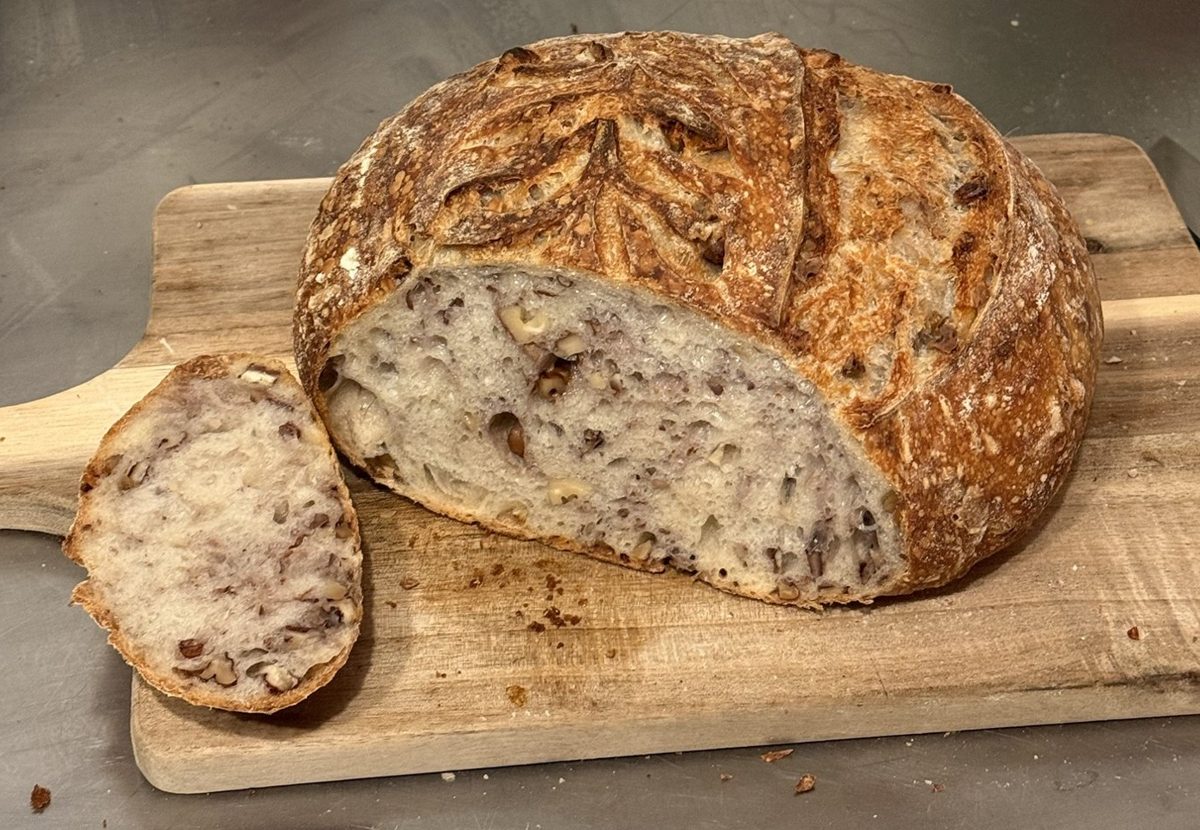 Sliced walnut pecan sourdough on a wooden board, showing walnuts and pecans throughout the tender crumb beside a thick slice